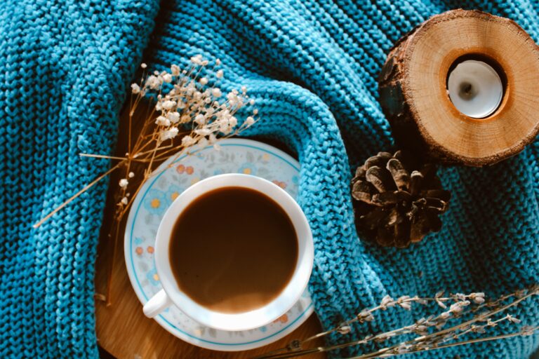 A cozy lifestyle setting featuring a warm latte mug, knit blanket, and unique holiday gifts for coffee lovers.